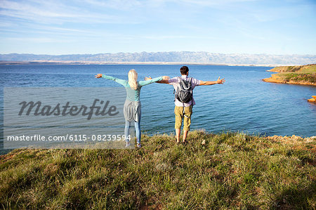 Young couple standing on cliff arms outstretched