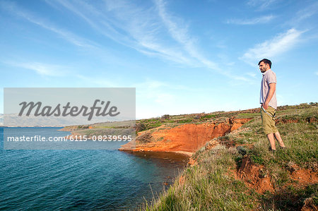 Young man stands on cliff looking at sea