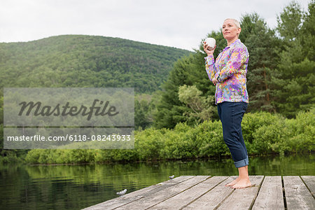 A woman standing on a lake dock holding a coffee cup.
