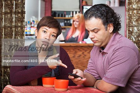 Annoyed woman pointing at cell phone held by man