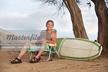 Single cheerful athletic male sitting with surfboard