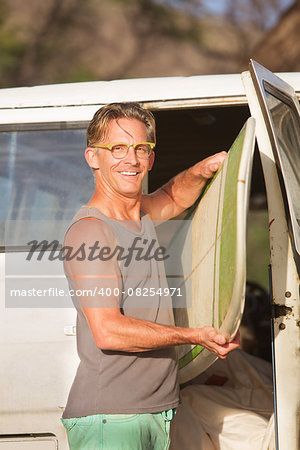 Smiling person with eyeglasses taking a surfboard from his van