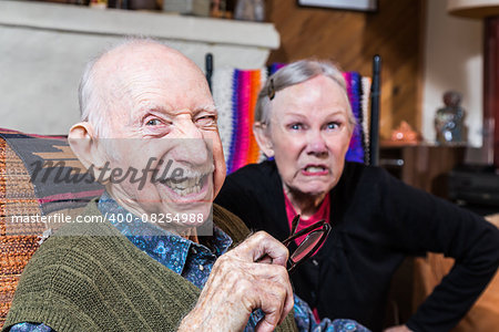 Angry old couple sitting indoors with scowling expression