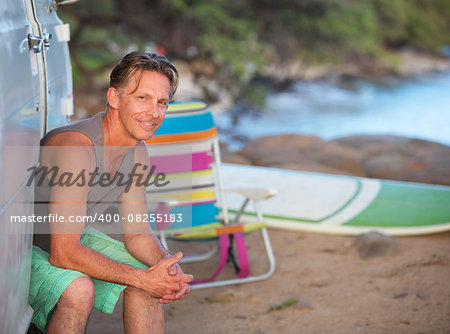 Male European surfer sitting in van door on beach