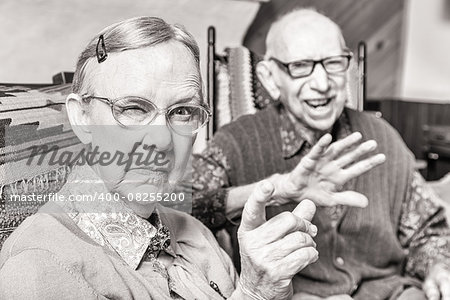 Toned image of angry old couple sitting in living room woman pointing