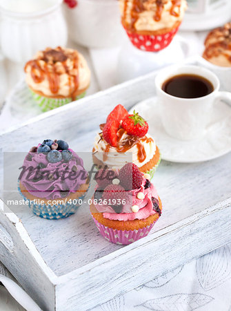 Different delicious cupcakes and coffee cup on white wooden tray