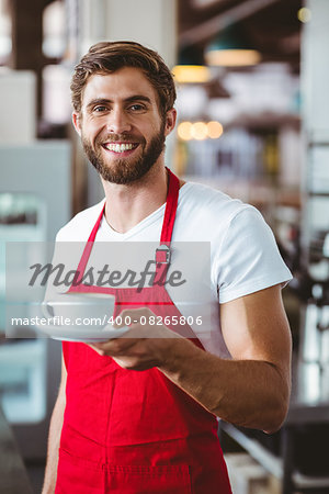 Handsome barista holding a cup of coffee at the cafe