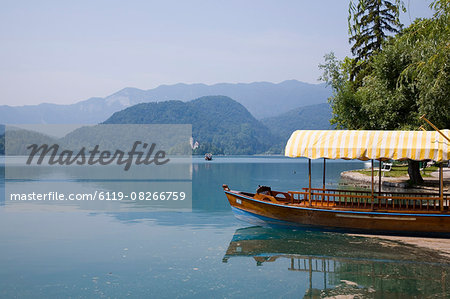 Traditional wooden pletnja (rowing boat) moored on shore to ferry tourists to St. Mary's Church of Assumption on the islet beyond, Lake Bled, Slovenia, Europe