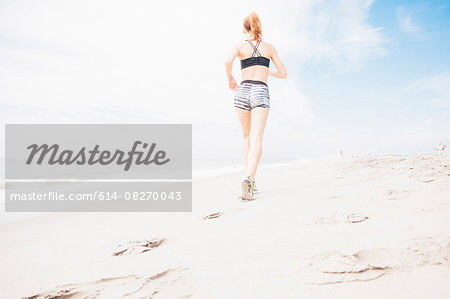 Mid adult woman power walking on beach, rear view, low angle view