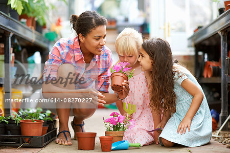 Mid adult woman and two girls smelling flower pots in greenhouse
