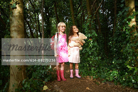 Two girls carrying teddy bear and backpack in forest