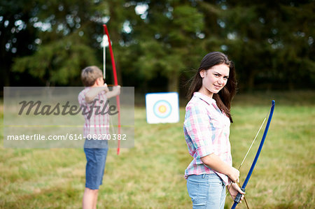 Portrait of teenage girl practicing archery with brother