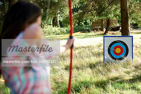 Rear view of teenage girl practicing archery with target