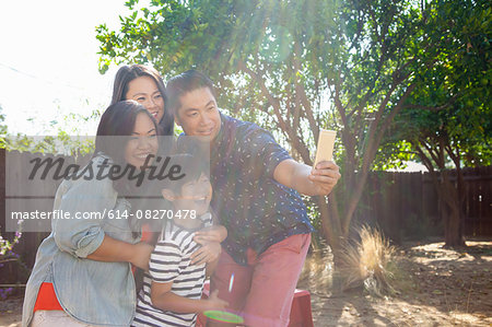 Family with boy posing for smartphone selfie in sunlit garden