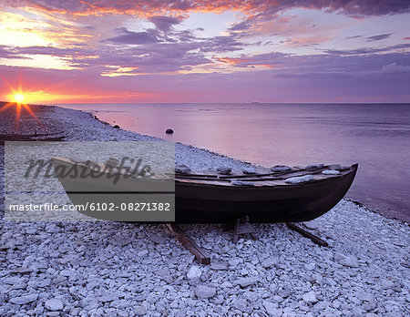 Rowboat on rocky beach at sunset
