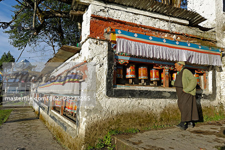 India, Arunachal Pradesh, Tawang. A local pilgrim turns prayer wheels (aka mani wheels) near the entrance to Tawang Monastery. Perched on a lofty ridge near the border with Bhutan and Tibet, the 17th century monastery is among the largest Tibetan Buddhist monasteries in India.