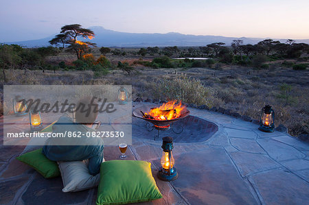 Kenya, Amboseli National Park, Tortilis Camp. A guest relaxes with a beer, overlooking Mount Kilimanjaro.