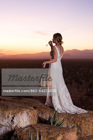 Kenya, Meru. A new bride enjoys a glass of Champagne, watching the sun set over Meru National Park.