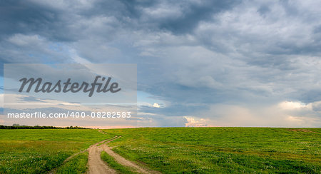 Rural road in the fields with dramatic sky before sunset landscape. Belarus.