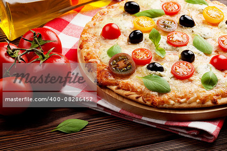 Italian pizza with cheese, tomatoes, olives and basil on wooden table