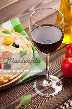 Glass of red wine and italian pizza with cheese, tomatoes, olives and basil