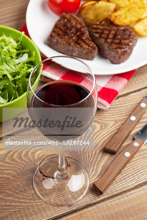 Glass of red wine and steak with salad on wooden table