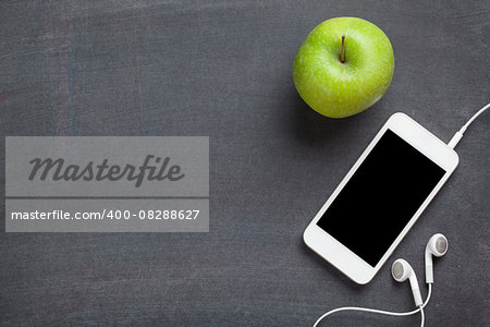 Smartphone and apple on blackboard background. Top view with copy space