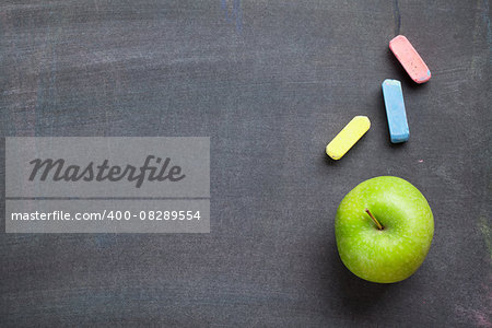 Colorful chalk and apple on blackboard background. Top view with copy space