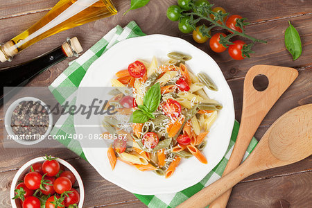 Colorful penne pasta with tomatoes and basil on wooden table. Top view