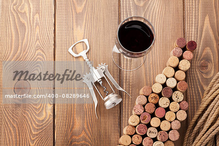 Wine bottle shaped corks, glass of wine and corkscrew over rustic wooden table background. View from above with copy space