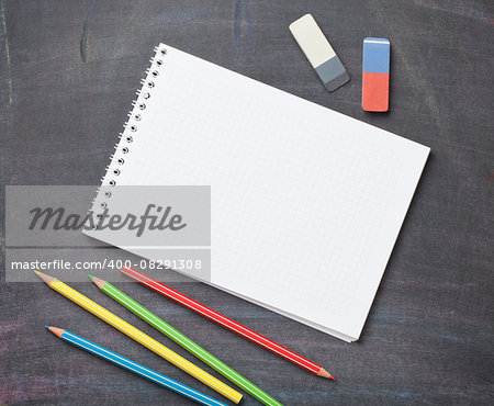 Blank notepad and colorful pencils on blackboard background. Top view with copy space