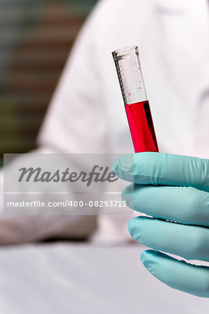 Closeup hand of chemist with a red liquid