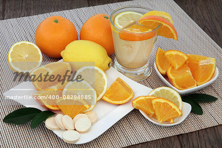 Cold and flu health remedy drink with orange and lemon fruit and vitamin c tablets on bamboo over oak background.