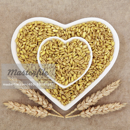 Kamut khorasan wheat grain health food in heart shaped porcelain dishes with sheaths over brown grunge paper background.