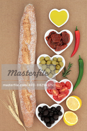 French baguette bread loaf with antipasti selection of fresh and sundried tomatoes, green and black olives, chilli peppers, olive oil and lemon halves.