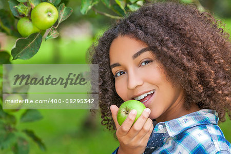 Outdoor portrait of beautiful happy mixed race African American girl teenager female child eating an organic green apple and smiling with perfect teeth