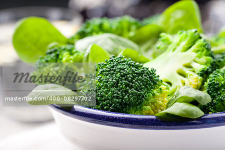Broccoli, baby spinach and green beans salad in ceramic bowl with olive oil on a white wooden background.