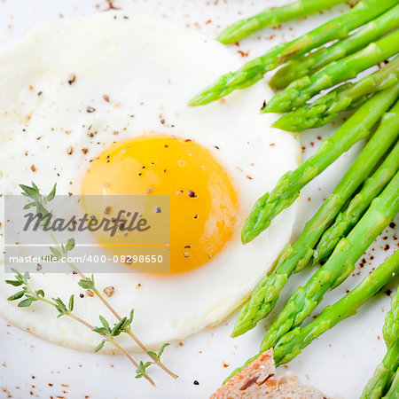 Green asparagus with fried egg and bread with butter on a white plate.
