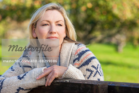 Attractive thoughtful middle aged woman leaning resting on fence in the countryside