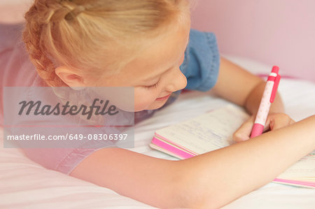 Cropped view of girl on bed writing in notebook