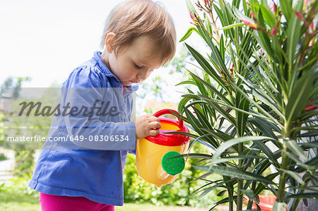 Female toddler watering plants with toy watering can in garden