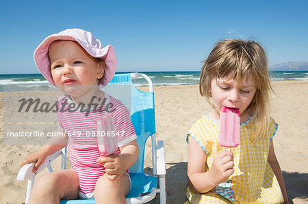 Female toddler and sister eating ice lollies on beach