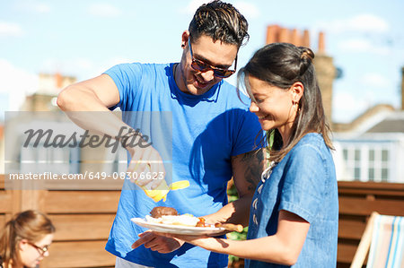 Mid adult man squirting mustard on burger at rooftop party