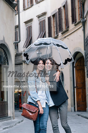 Lesbian couple standing together in street holding umbrella looking at camera smiling, Florence, Tuscany, Italy