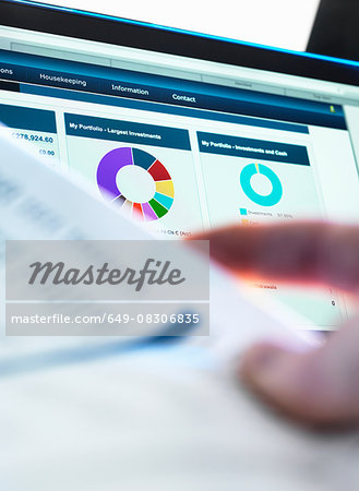 Investor checking performance of financial portfolio online whilst reviewing investment statement Investor checking performance of financial portfolio online whilst reviewing investment statement