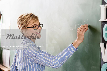 Female teacher in classroom, writing on blackboard