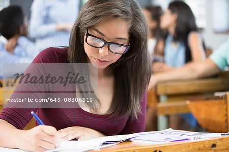 Female student, sitting at desk in classroom, writing