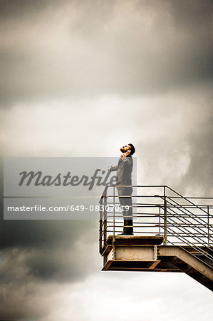 Low angle side view of mid adult man on stairs wearing suit, arms open thowing head back