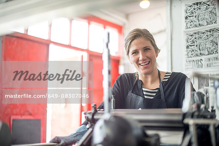 Portrait of female printer with traditional letterpress print machine in workshop