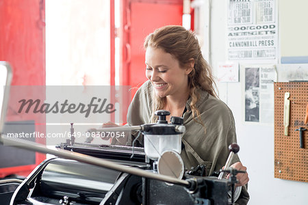 Female letterpress printer preparing printing machine in workshop